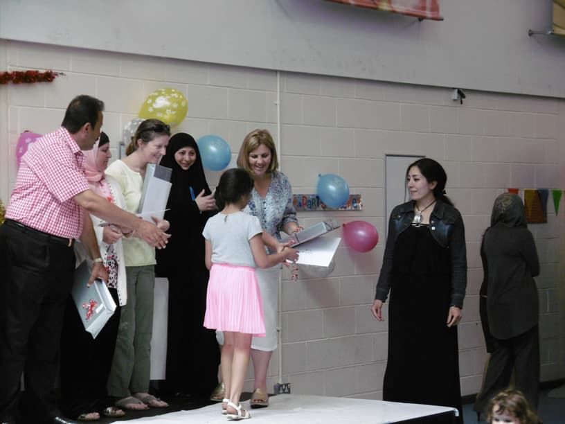 Children and parents at a Babylon Academy prize-giving celebration, with a pupil receiving a certificate.